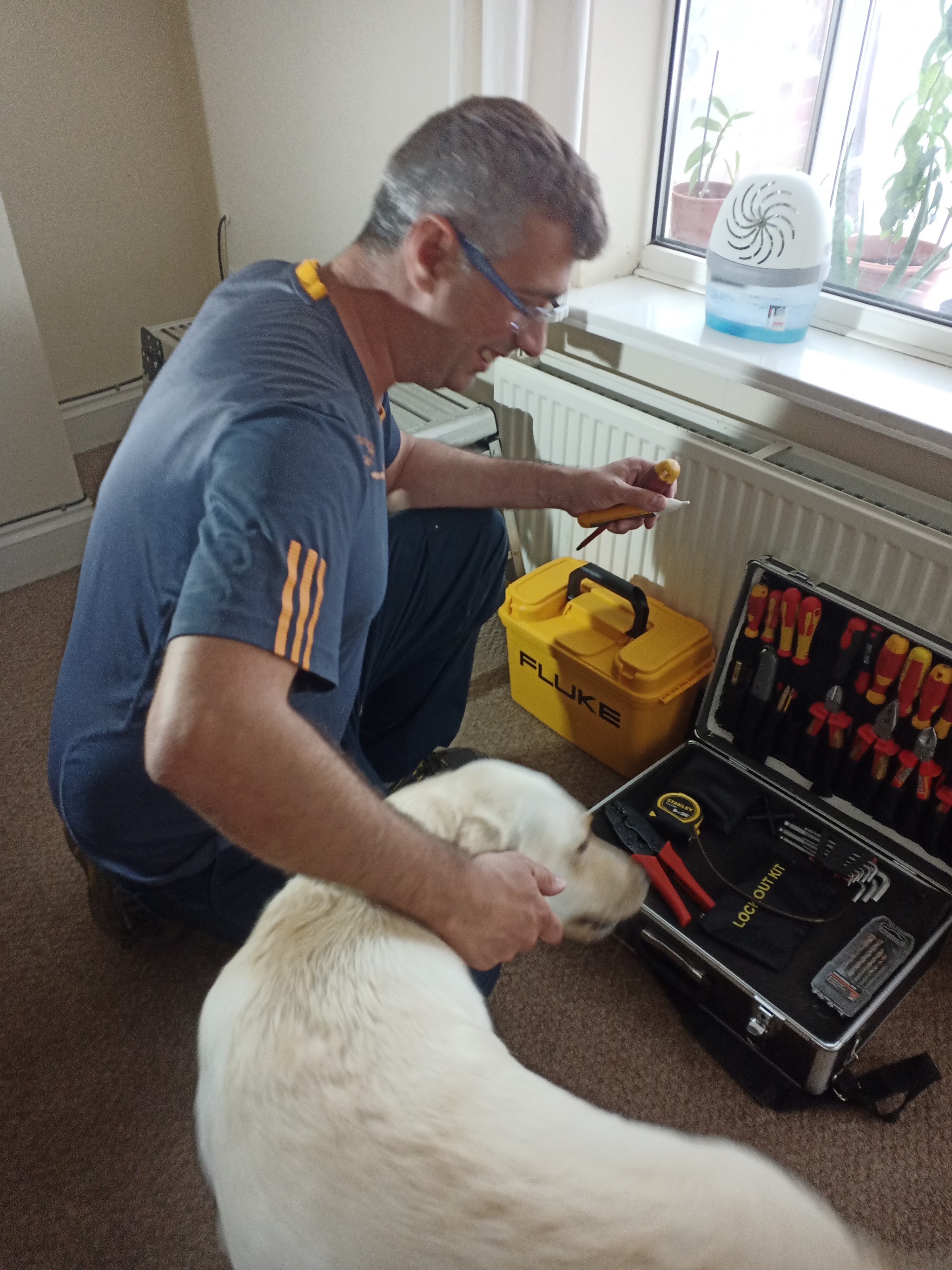 Our electrician kneeling by his open tool case in a customer's home, saying hello to the family dog